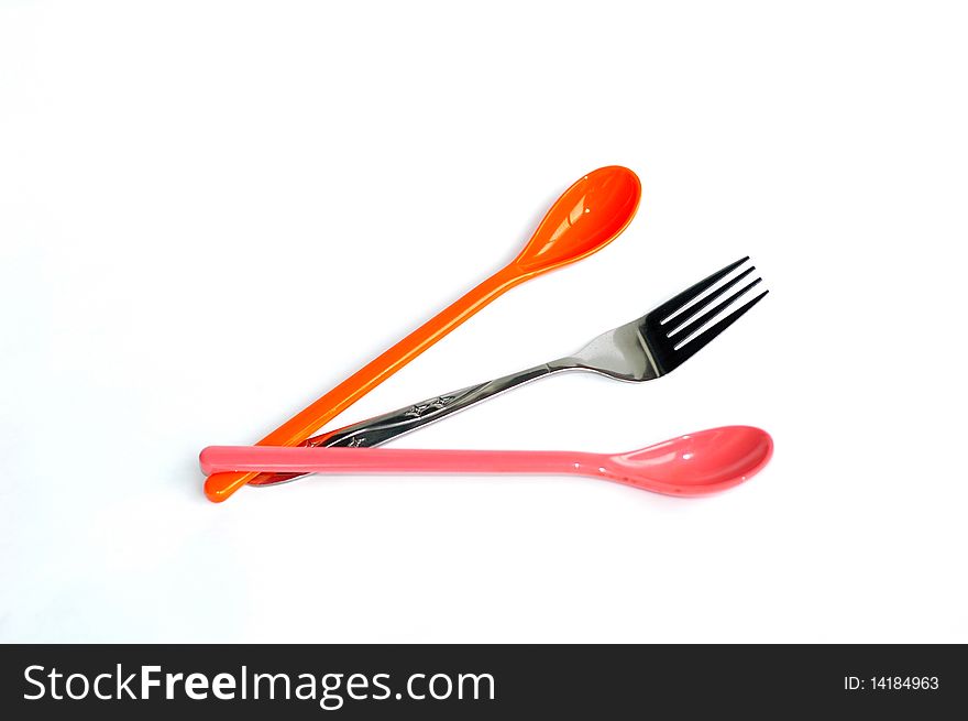 A pair of colorful plastic spoons with a stainless steel fork in the middle isolated on white background. A pair of colorful plastic spoons with a stainless steel fork in the middle isolated on white background