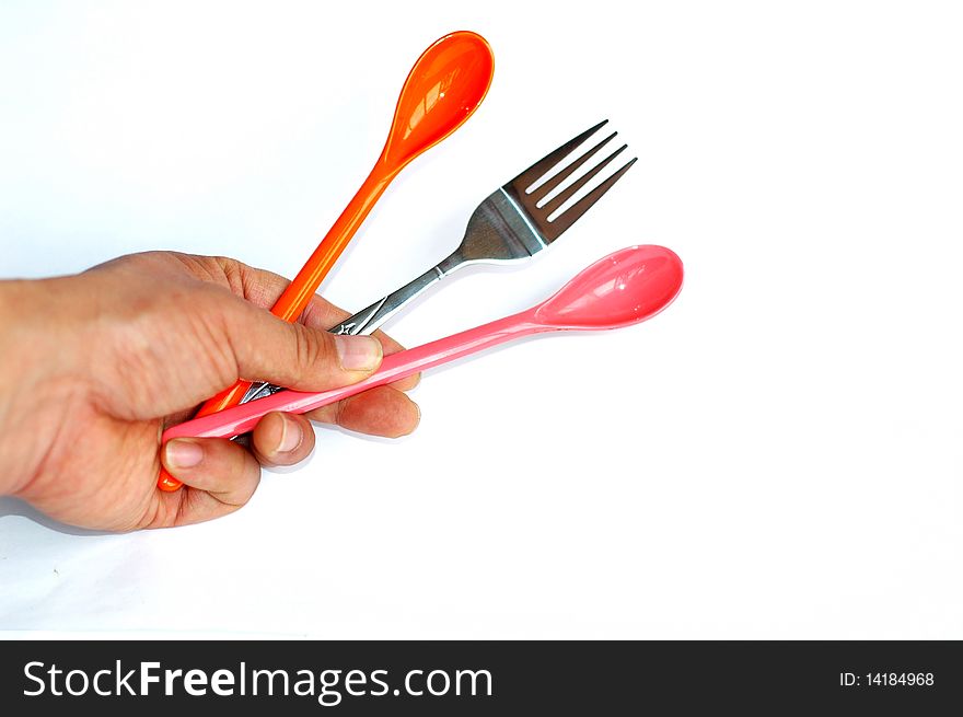 A pair of colorful plastic spoons with a stainless steel fork in hand isolated on white background. A pair of colorful plastic spoons with a stainless steel fork in hand isolated on white background