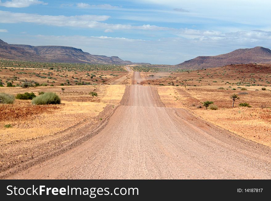 Straight sandy road through Namibian landscape with blue cloudy sky. Straight sandy road through Namibian landscape with blue cloudy sky.