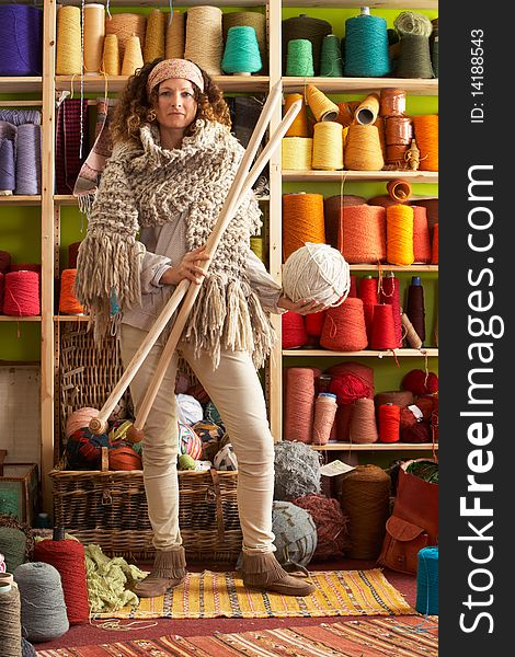 Woman Wearing Knitted Scarf Standing In Front Of Yarn Display Holding Giant Needles