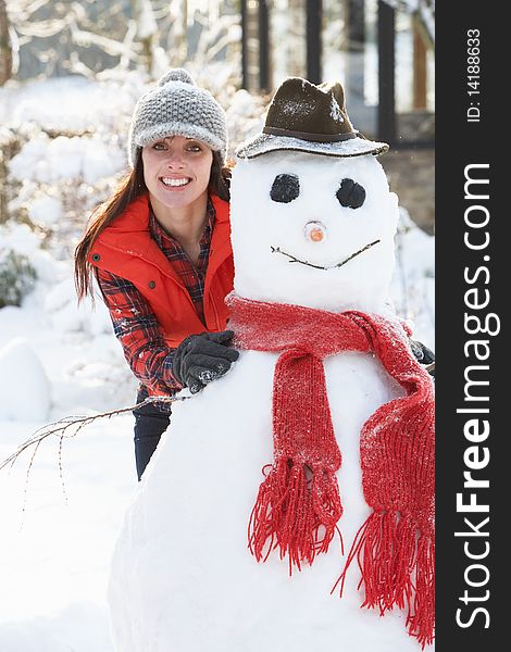 Young Woman Building Snowman In Garden