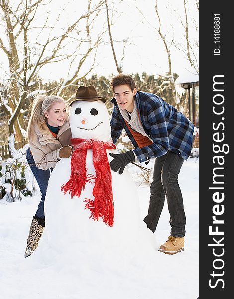 Teenage Couple Building Snowman Looking At Camera