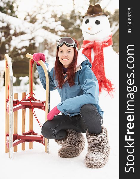 Teenage Girl With Sledge Next To Snowman