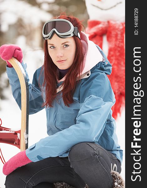 Teenage Girl With Sledge Next To Snowman Looking At Camera