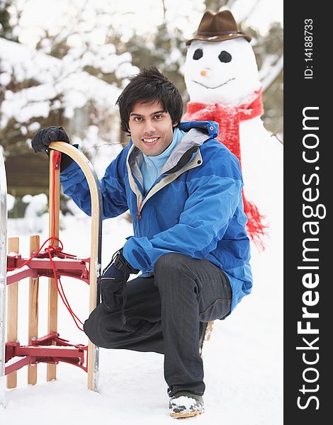 Smiling Teenage Boy With Sledge Next To Snowman