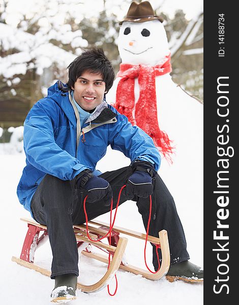 Smiling Teenage Boy With Sledge Next To Snowman