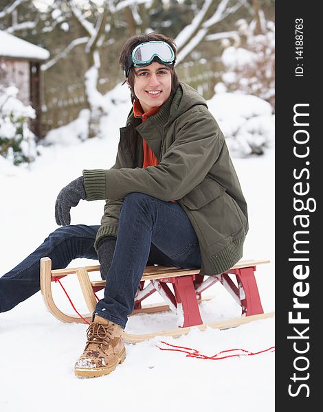 Teenage Boy With Sledge Next To Snowman Smiling At Camera