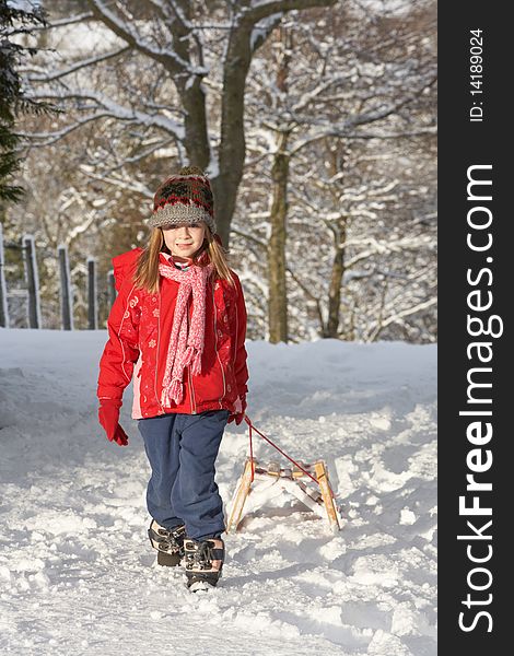 Young Girl Pulling Sledge Through Snowy Landscape looking at camera