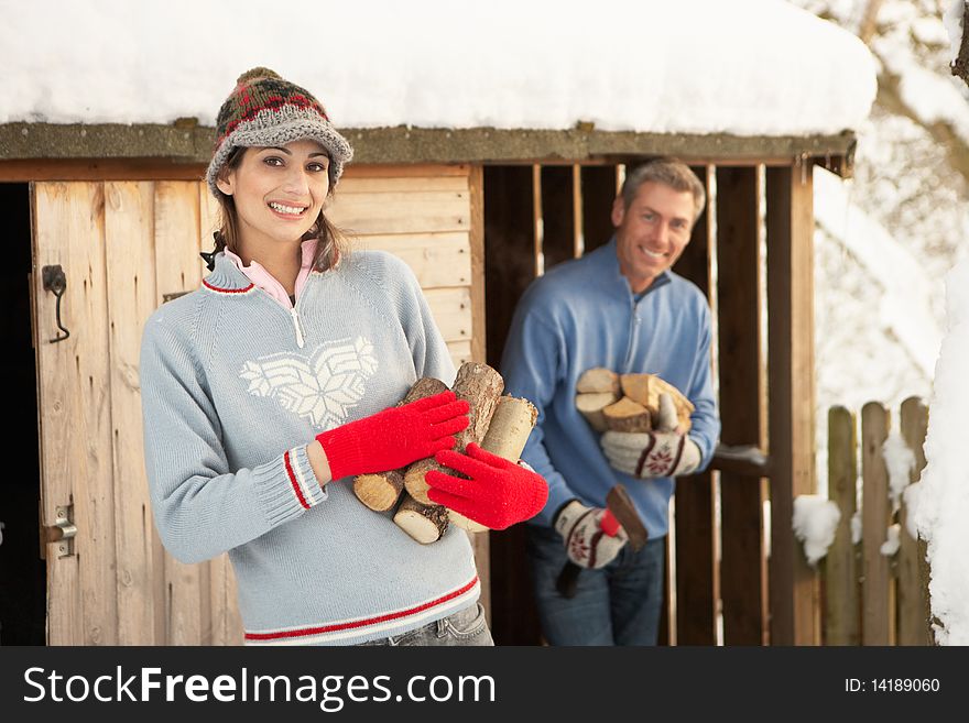 Young Couple Collecting Logs From Wooden Store In Snow