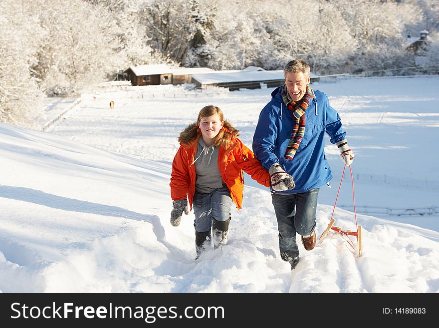 Father And Son Pulling Sledge Up Snowy Hill Having Fun