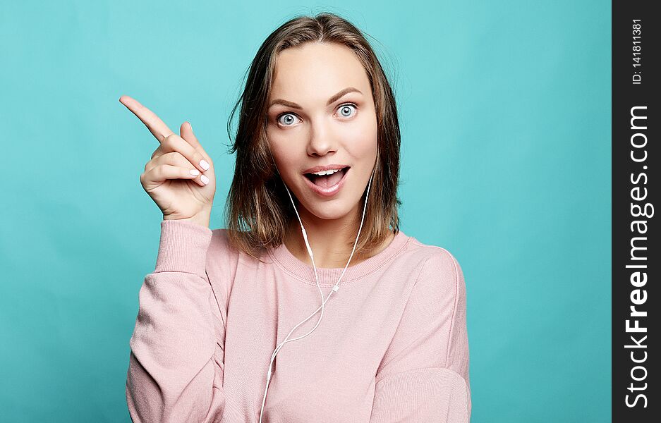 Surprised funny woman showing empty copy space with her finger. Happy girl pointing, looking at camera.