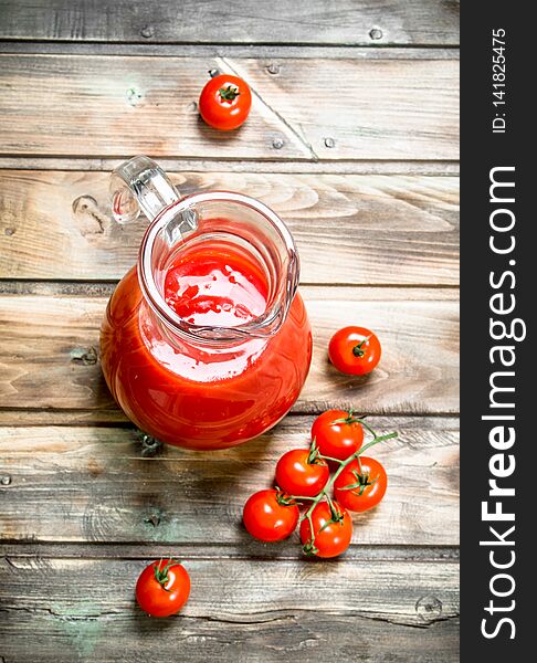 Tomato juice in a jug and fresh tomatoes. On wooden background