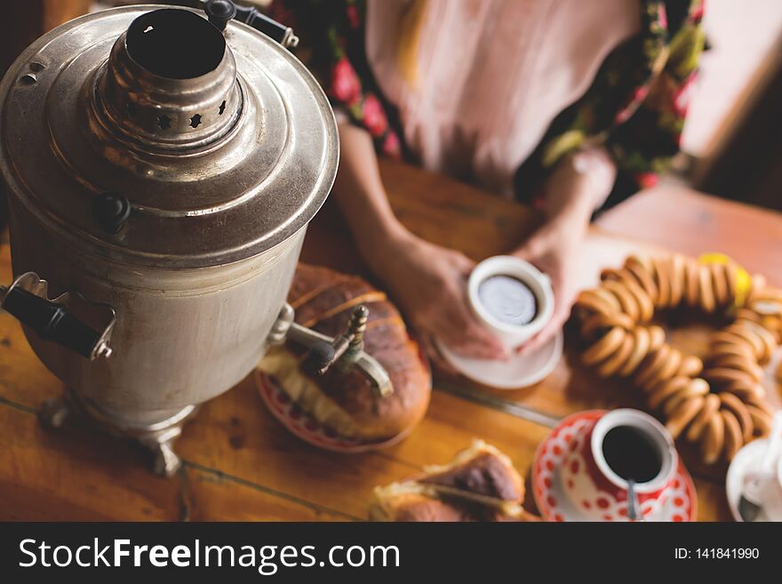 Tea, traditional Russian dishes and treats, a samovar on the table, the hands of a woman in a national kerchief are holding a cup of tea, Moskow