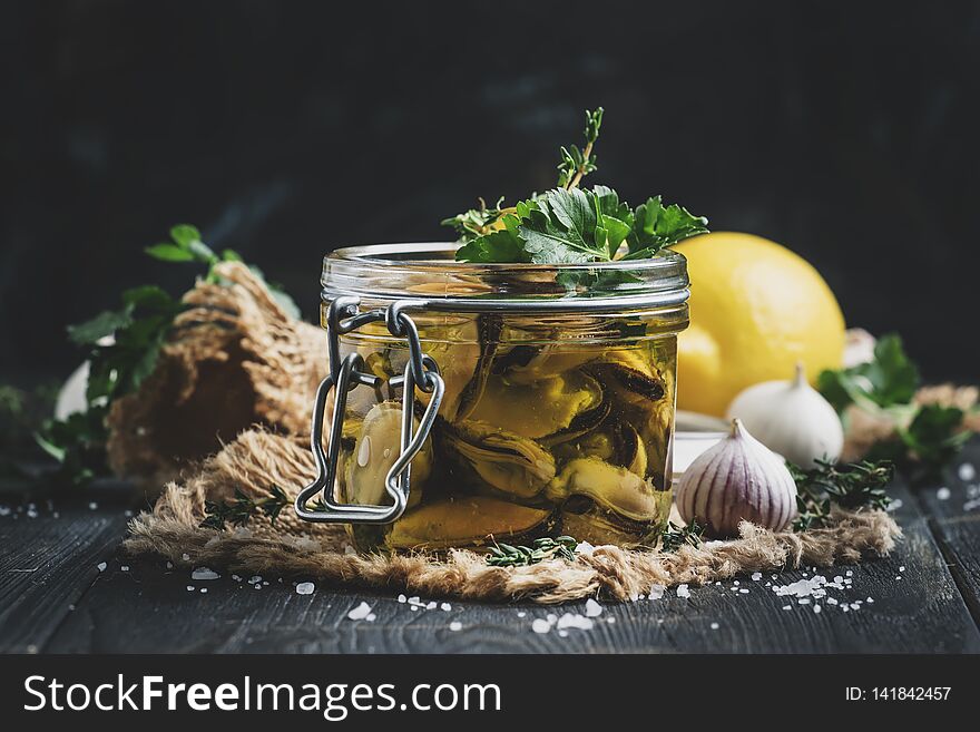 Canned mussels in olive oil and lemon juice with spices, garlic and herbs, black wooden kitchen table, selective focus