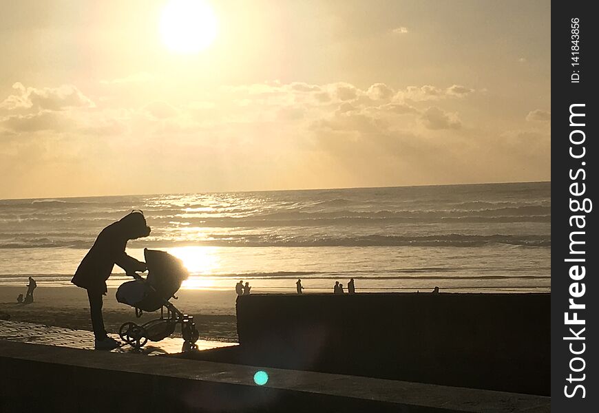 Mother love with small kid in baby carriage on the beach with romantic sunset.