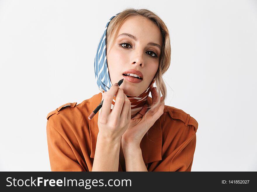 Beautiful young woman wearing silk stylish scarf posing isolated over white wall background apply makeup with lip pencil