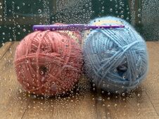 Blue And Pink Skeins Of Wool With A Purple Crochet Hook. Seen Through A Window With Raindrops Stock Images