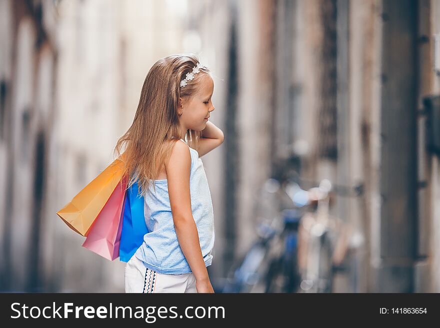 Portrait of adorable little girl walking with shopping bags outdoors in european city.