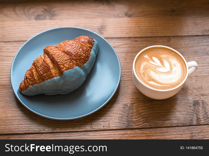 Cup of fresh cappuccino art and croissant on wooden background.