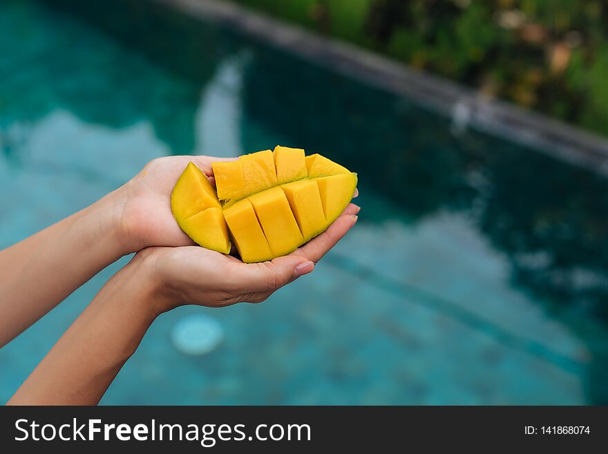 Close up slice of mango in female hands on background of blue swimming pool.