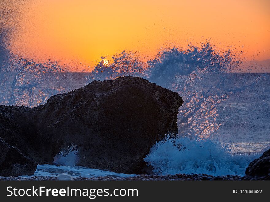 Sea waves crushing and splashing on the rocks on a tropical beach, in beautiful warm sunset light