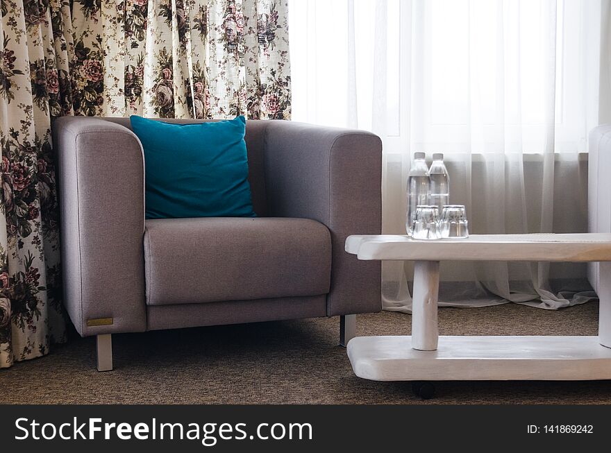 Interiors of the room in the hotel concept. A sofa with a blue pillow and a white table with water bottles.