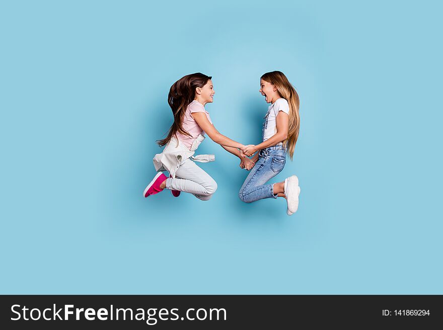 Full length body size profile side view of two people nice cute attractive cheerful straight-haired pre-teen girls having fun great weekend holding hands isolated over blue pastel background.