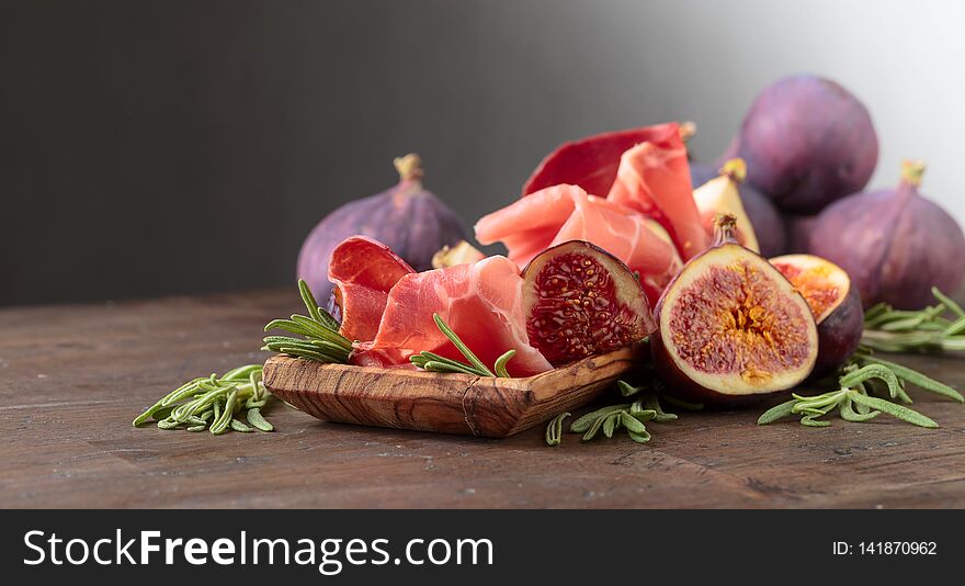 Prosciutto with figs and rosemary on a old wooden table. Traditional Italian food made from dried pork