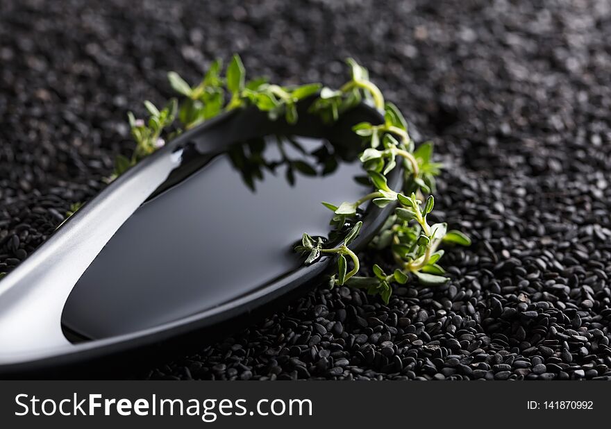 Vegetable oil in small bowl with thyme branches on a background of black sesame. Selective focus