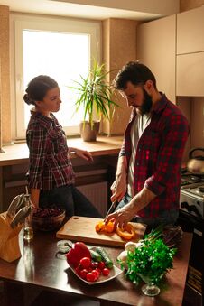 Beautiful Young Couple In Kitchen At Home While Cooking Healthy Food. Man Cuts A Pepper. Woman Looks At Her Husband. Scene From Royalty Free Stock Image