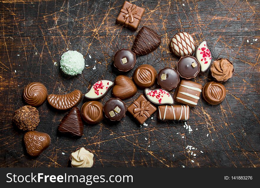 Chocolate sweets with nuts and various fillings. On a wooden background