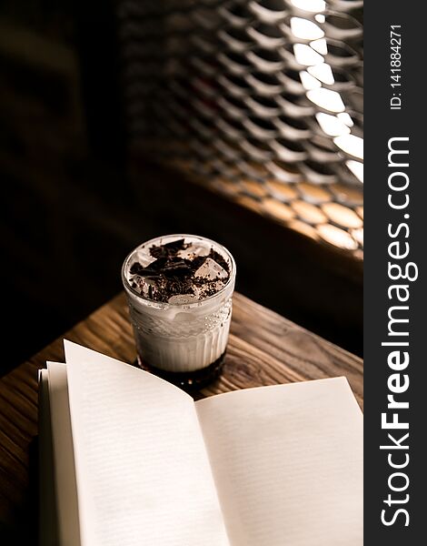 Close-up on a brown wooden table with coffee and cream, next to it is a book. Close-up on a brown wooden table with coffee and cream, next to it is a book.