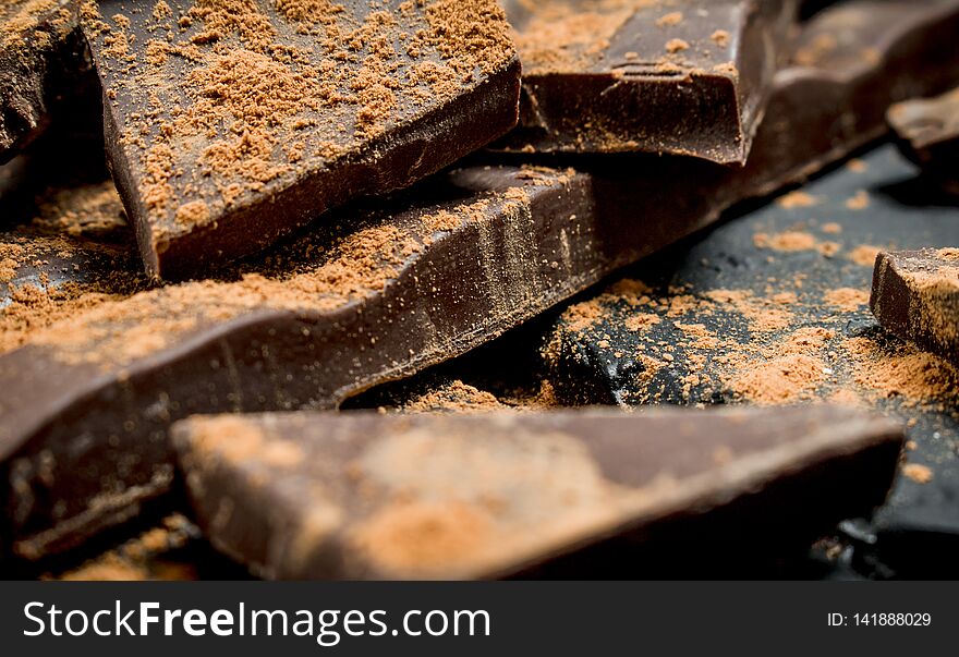 Chocolate slices sprinkled with cocoa powder. On black rustic background