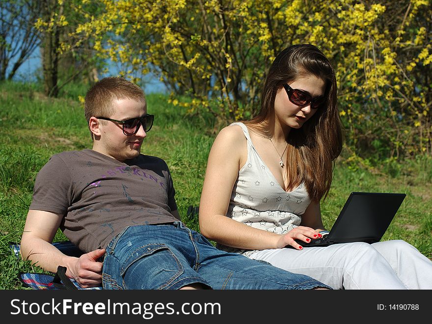 Young couple with laptop outdoors on the spring meadow