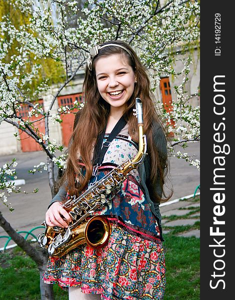 Beautiful smiling girl with saxophone, spring tree