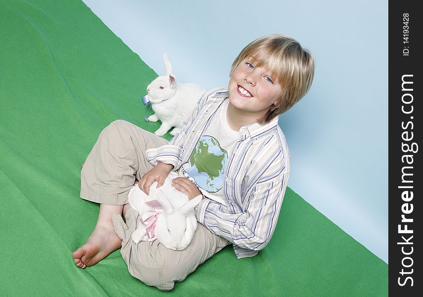 A young lad sitting with his legs crossed on the floor with two white rabbits. A young lad sitting with his legs crossed on the floor with two white rabbits