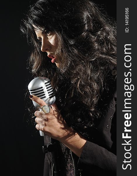 Portrait of young beautiful brunette woman singing with retro microphone - isolated on black. Portrait of young beautiful brunette woman singing with retro microphone - isolated on black