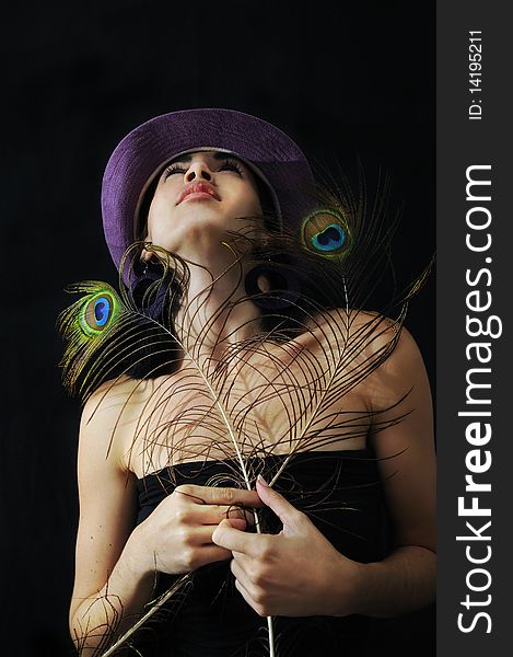 Portrait of young trendy girl holding peacock feathers against black background. Portrait of young trendy girl holding peacock feathers against black background