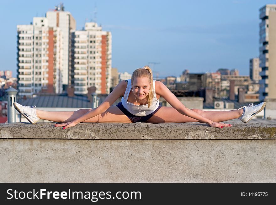 Blond gymnastic girl smiling and posing on a roof with buildings in background