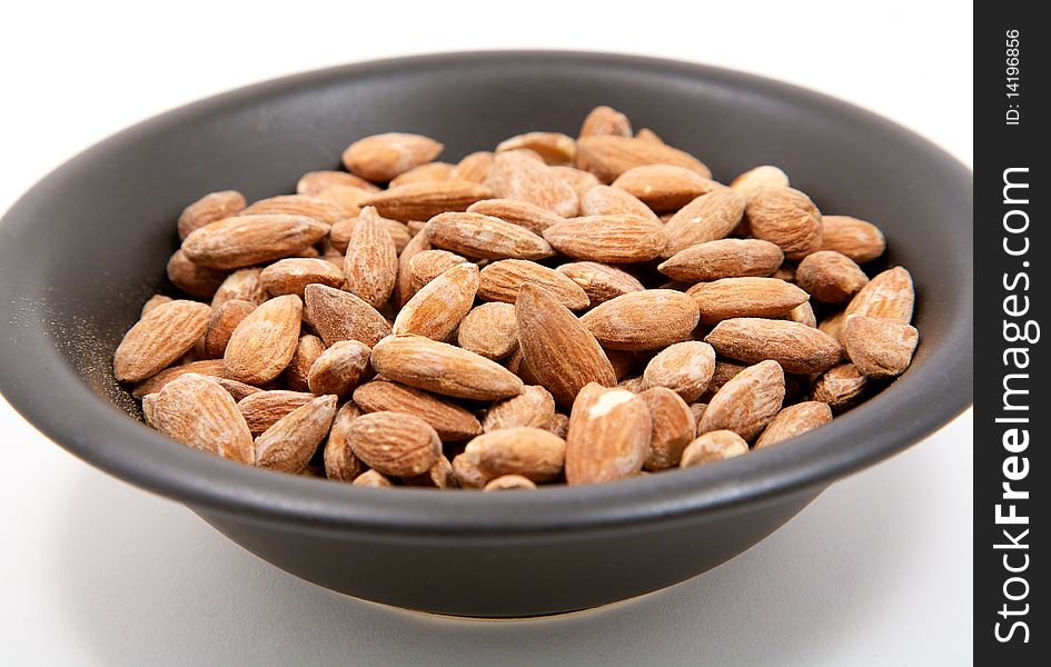 A black bowl full of salted almonds isolated on a white background. A black bowl full of salted almonds isolated on a white background