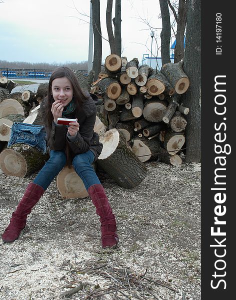 Young beautiful teenage girl sitting on logs with a mobile phone