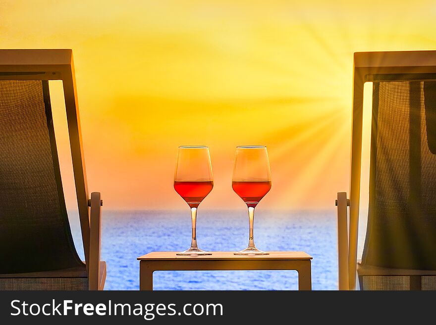 Two glasses of red wine in the sun rays at sunset. Two summer chairs and a table with two glasses of red wine at sunset. Toning. Two glasses of red wine in the sun rays at sunset. Two summer chairs and a table with two glasses of red wine at sunset. Toning