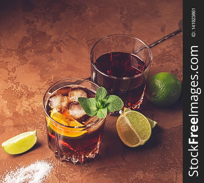 Cocktail of rum and cola ice cubes and lime in glass goblets on a dark brown background. Strong alcoholic drink.