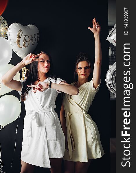 Portrait of strong and dangerous women with make up posing at camera. Gorgeous brunette girls holding their hands up and dancing. Happy friends chilling out at party near white and gold balloons. Portrait of strong and dangerous women with make up posing at camera. Gorgeous brunette girls holding their hands up and dancing. Happy friends chilling out at party near white and gold balloons.