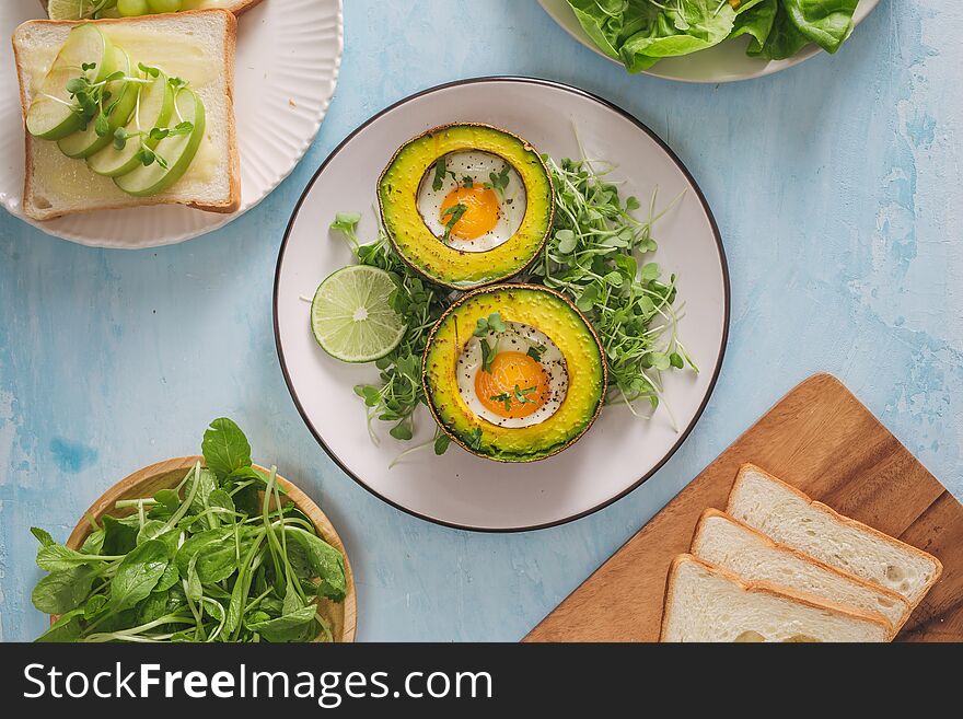Healthy vegan breakfast. Diet. Baked avocado with egg and fresh salad from arugula, toast and butter. On a white marble plate, a