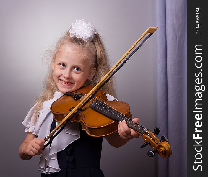 Happy little girl playing the violin on gray background g