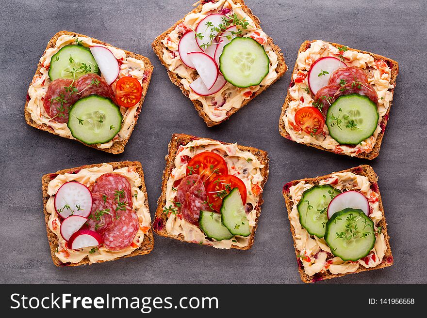 Sandwiches with cream cheese, vegetables and salami. Sandwiches with cucumber, radish, tomatoes, salami on a gray background, top view. Flat lay