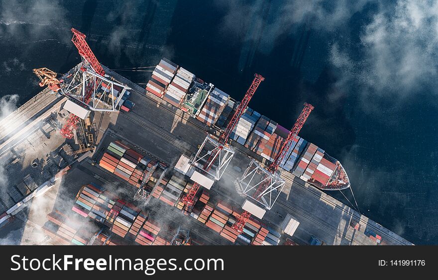 Top view of a cargo ship with containers, which is unloaded in the port. Container Warehouse, Logistics, Cranes, Outdoor, Import and export. Top view. Top view of a cargo ship with containers, which is unloaded in the port. Container Warehouse, Logistics, Cranes, Outdoor, Import and export. Top view