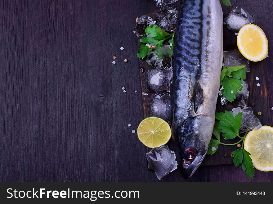 Fresh mackerel on a black chopping board surrounded by ice, lime, lemon, parsley and spices