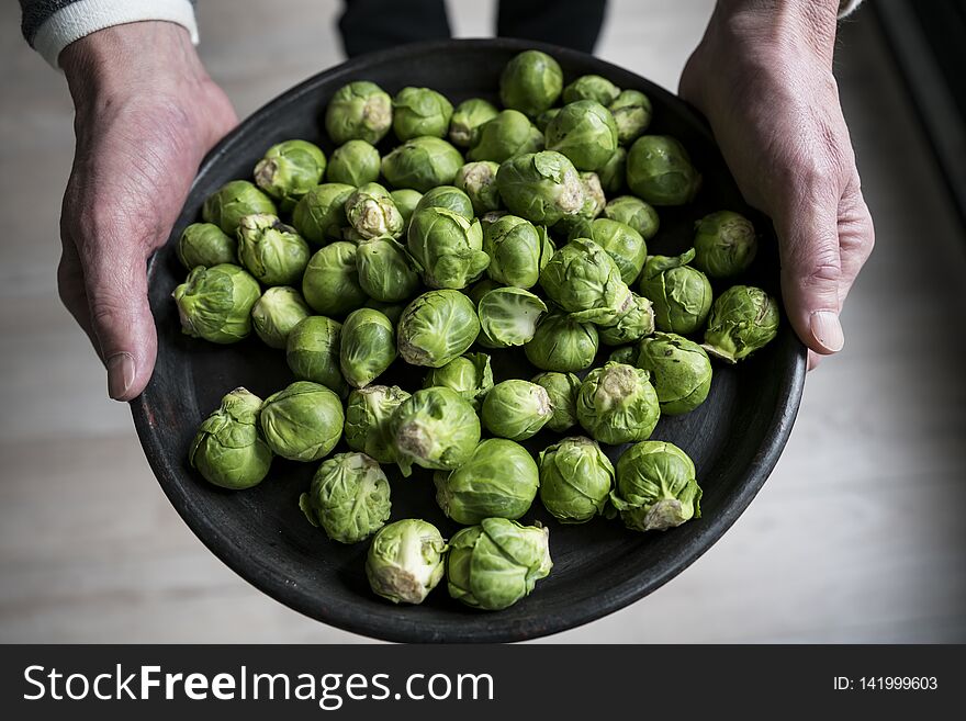 Man holding a black plate full of raw Brussels sprouts. Man holding a black plate full of raw Brussels sprouts.